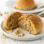 A perfect gluten free lentil bread roll sliced in half on a white plate.