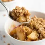 A close-up spoonful of gluten free apple crisp, showing the crunchy oat topping and soft apple filling.