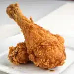 A single, perfectly crispy gluten free fried chicken drumstick against a white background.