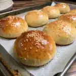 Proofed gluten free hamburger buns that have doubled in size, topped with egg wash and sesame seeds, ready to bake.