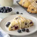 A single, flawless gluten free blueberry scone with a vanilla icing drizzle on a plate.