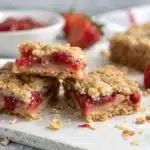 A close-up of a Strawberry Oatmeal Crumble Bar broken in half showing the gooey filling.