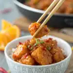 A close-up of a single piece of Gluten Free Orange Chicken held by chopsticks.